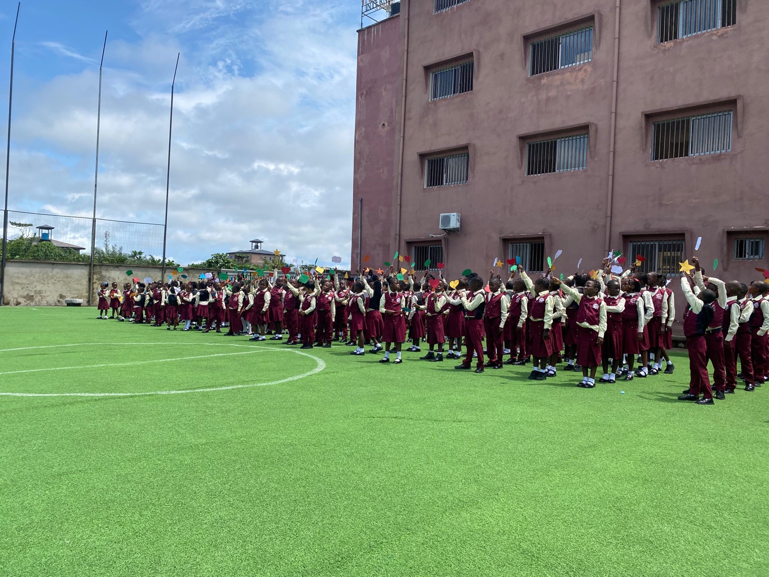 Pupils gathered on the school field holding colorful paper shapes